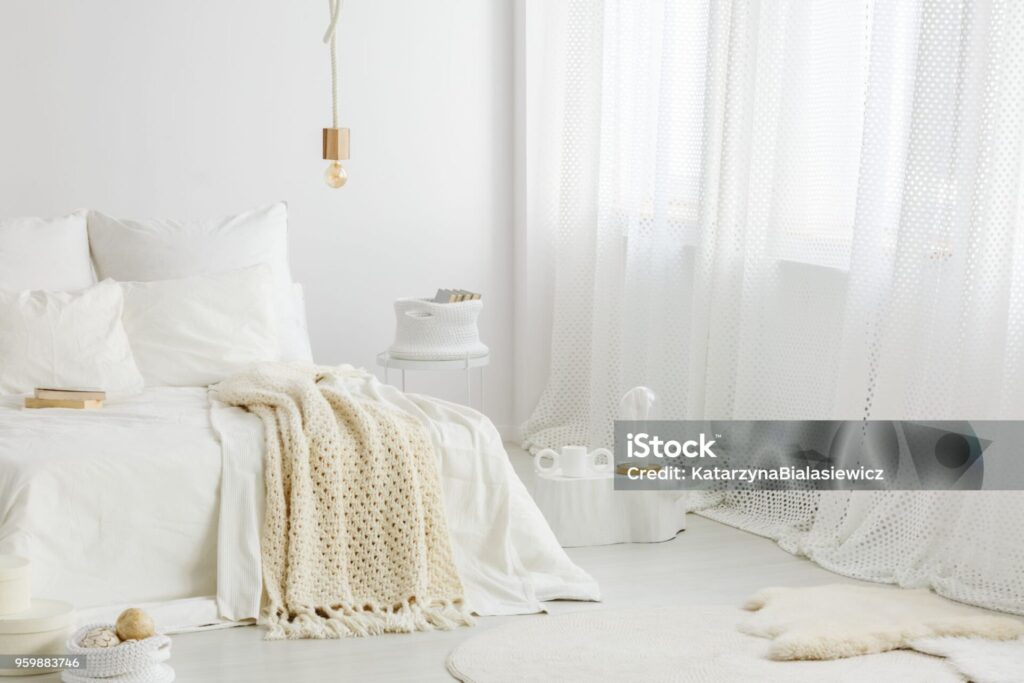 cozy, knit blanket on white bed in bright bedroom interior with a big window