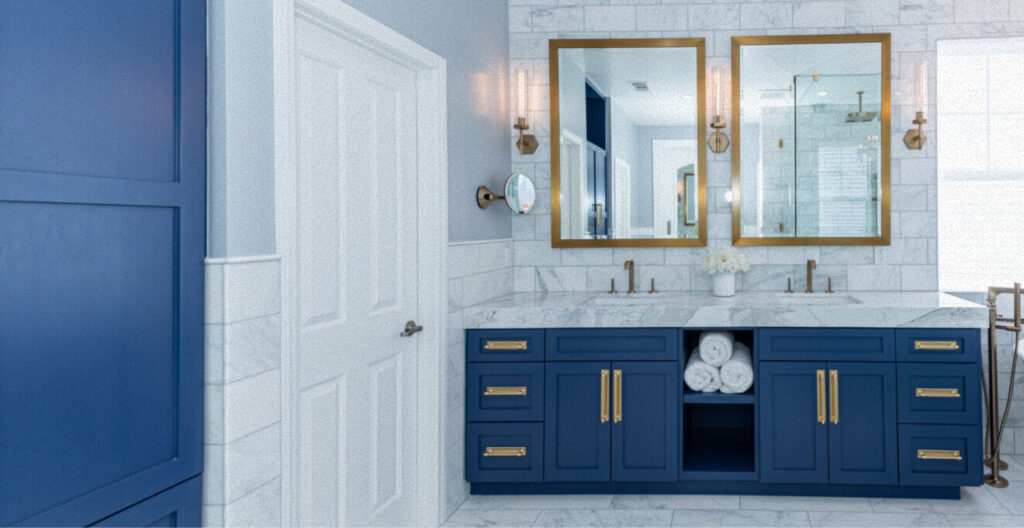 Elegant bathroom with a modern design, featuring blue cabinets with gold handles. Two large mirrors sit above a marble countertop.